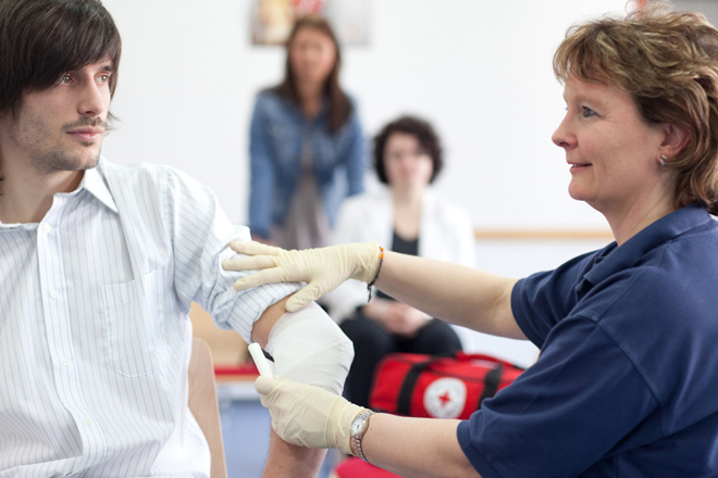 Eine Mitarbeiterin des DRK zeigt wie man einen Verband an legt an einem Teilnehmer 